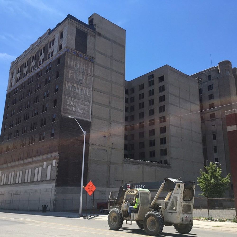 Schnappschuss eines gigantischen, leerstehenden Detroiter Gebäudekomplexes, der früher ein Hotel beherbergte. Auf der Straße vor dem verlassenen Gebäude verrichtet ein Bagger Straßenarbeiten.