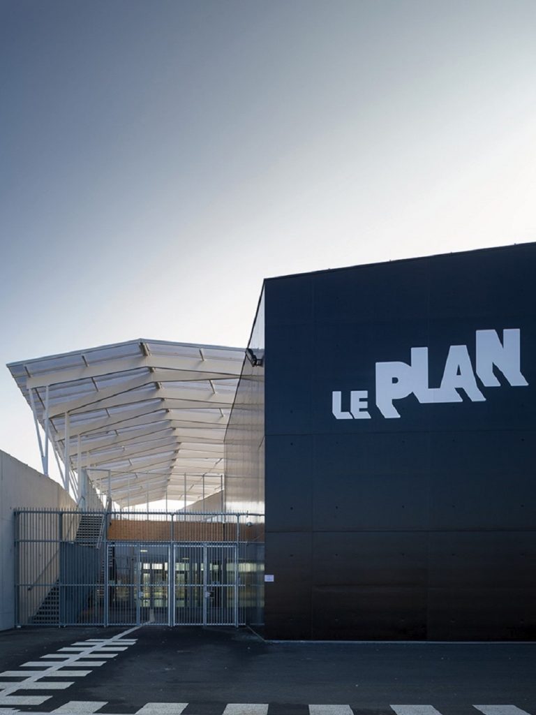 Photo of the Le Plan premises. The building resembles a black cube. On the left is a gated entrance to the building, on the right side the building is marked distinctively with the lettering Le Plan.