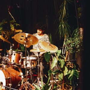 Dylan Hunter Chee Greene am Schlagzeug, umrahmt von Topfpflanzen
